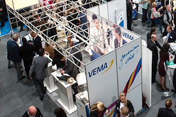 VEMA Messestand mit Besuchern, Beratungstischen und Metallgerüst auf einer Fachmesse